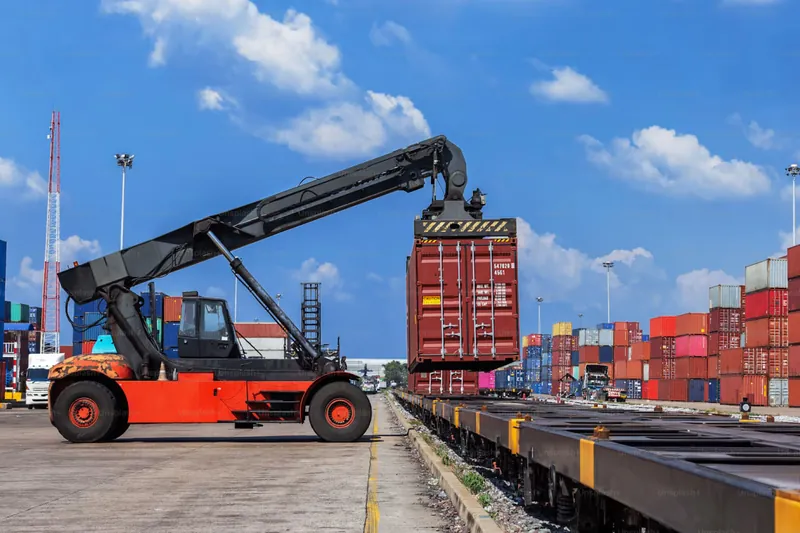 Grúa portacontenedores levantando un contenedor en un patio portuario, tema de FOB o CIF al importar a Chile